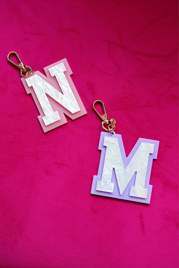 Set of two colorful acrylic letter keychains, 'N' in pink and 'M' in lavender with rose gold clips.