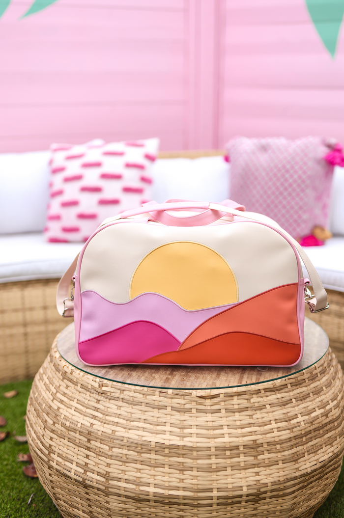 Colorful faux leather weekender bag with sunset design in pink, orange, and cream tones.
