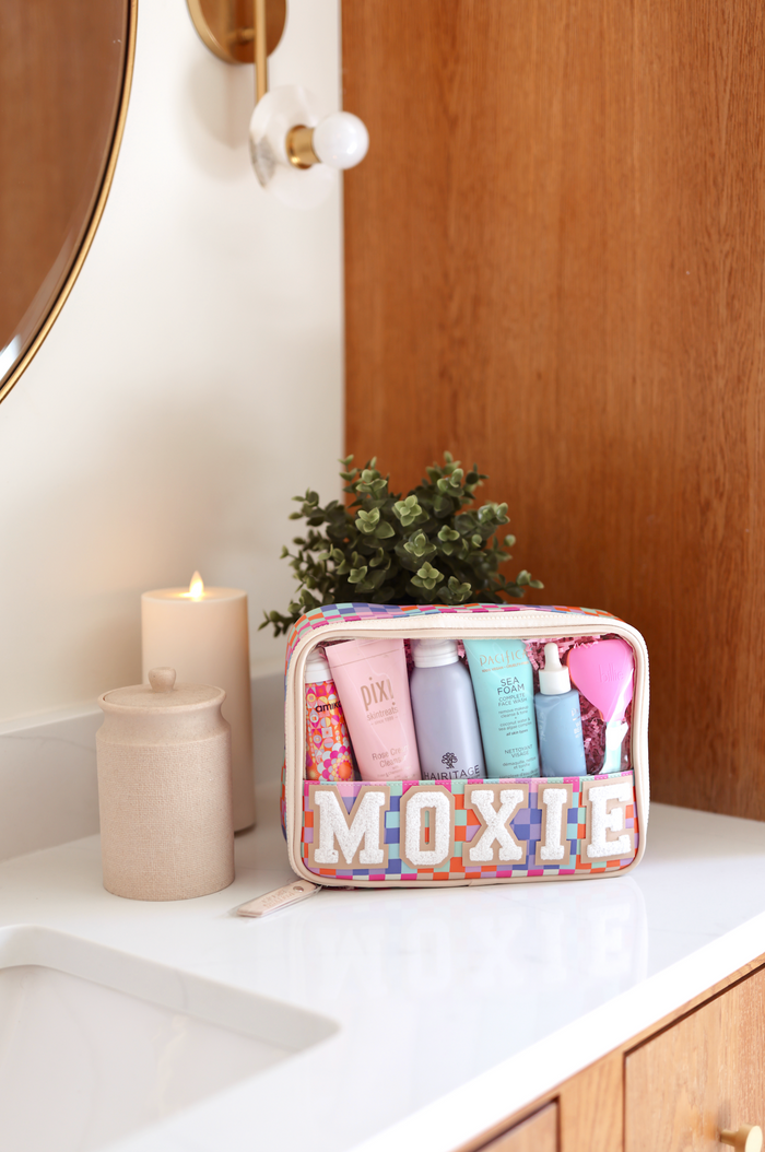 Colorful Moxie cosmetic bag filled with skincare products on a bathroom countertop.