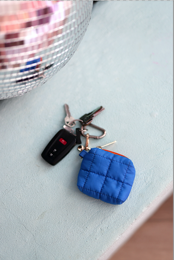 Small blue quilted keychain wallet with orange zipper on table next to car keys.