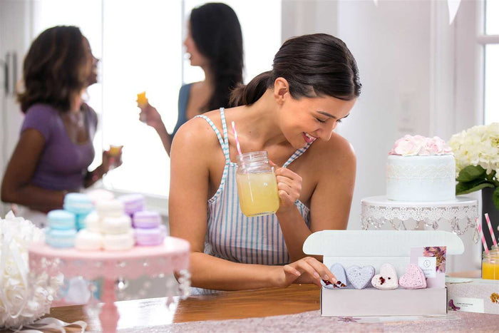 Woman drinking from a glass next to an exposed arrangement of Lizush natural shower steamers on a table