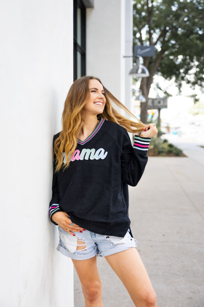 Black corded sweatshirt with 'Mama' lettering, featuring colorful striped collar and cuffs, stylish casual outfit.