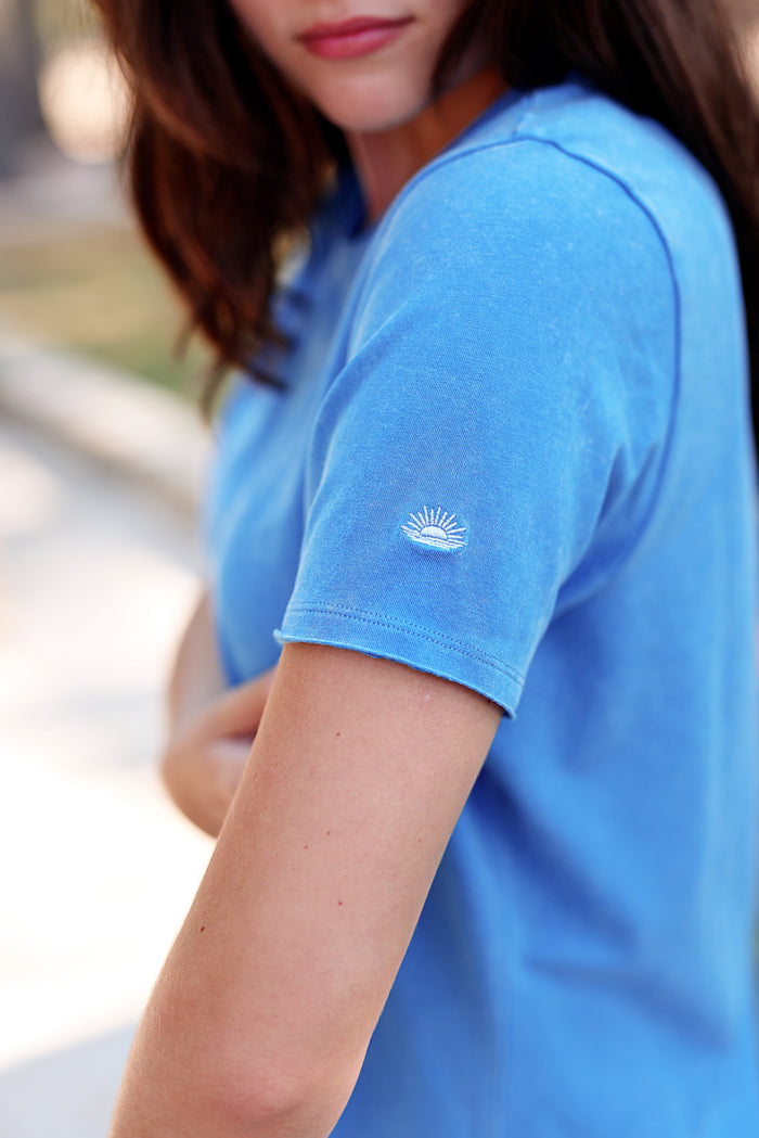 Light blue cotton t-shirt featuring an embroidered sun logo on the sleeve, perfect for casual wear.