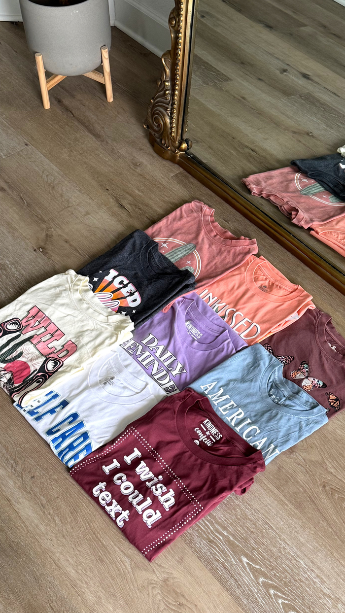Assorted graphic tees in various colors and designs, featuring playful slogans and casual style.