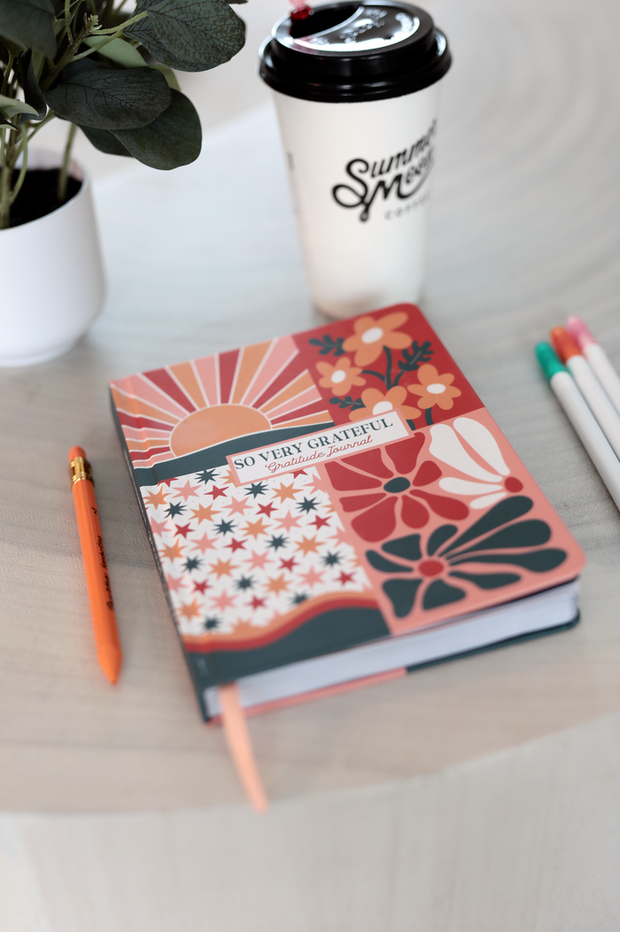 Colorful gratitude journal with floral design, featuring an orange pen on a wooden table.
