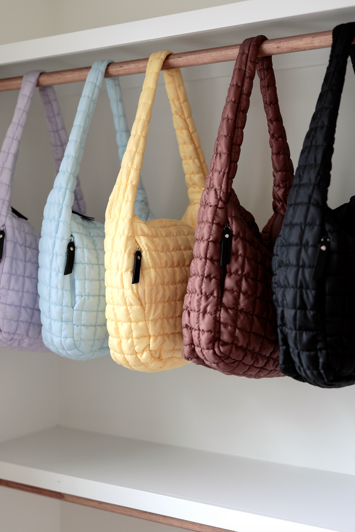 Colorful quilted handbags in purple, blue, yellow, brown, and black hanging on a rack.