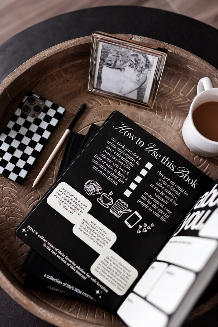 Black journal with instructions, surrounded by coffee and decor on wooden tray.