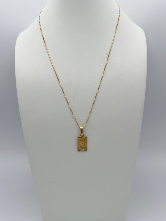 Gold chain necklace with rectangular pendant featuring engraved celestial design displayed on white jewelry bust