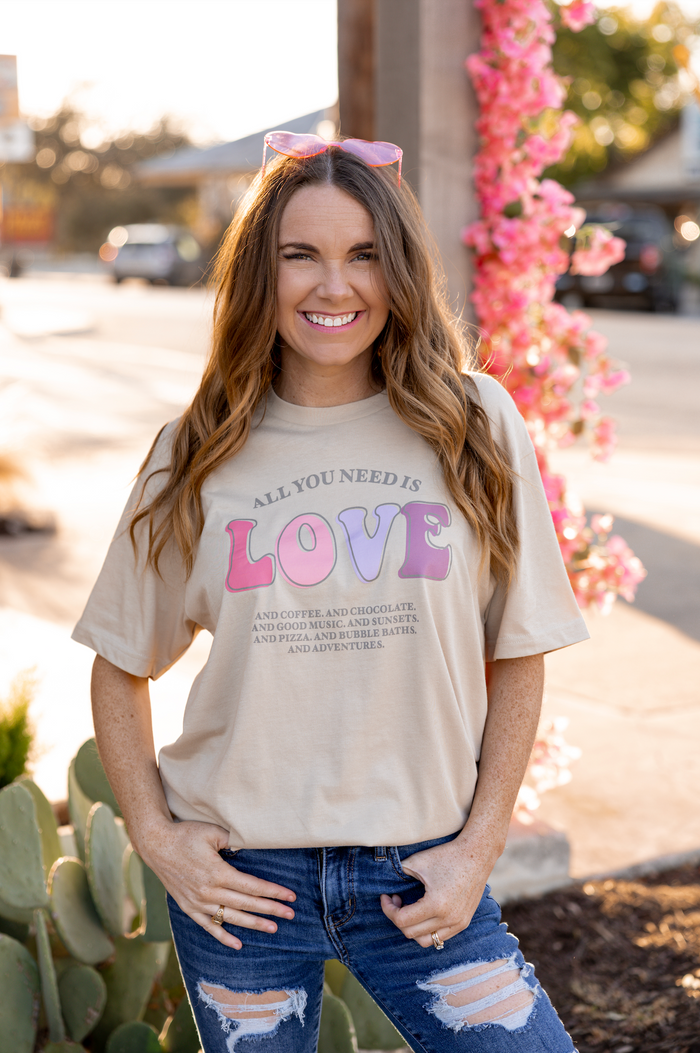 Beige graphic tee with 'All You Need Is Love' text, soft cotton material, styled with jeans.