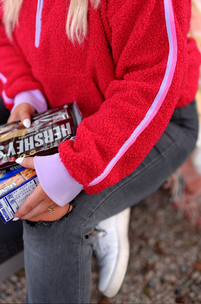 Cozy red fleece pullover with pink accents, held over jeans while clutching Hershey's snacks.