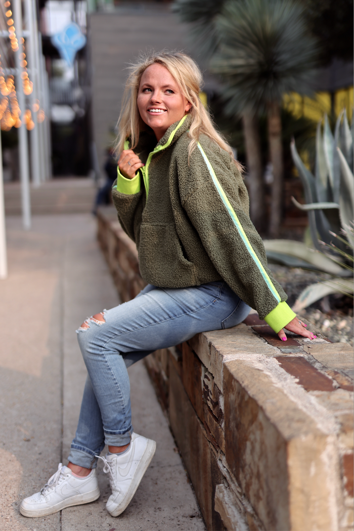 Cozy olive green fleece pullover with neon green accents, paired with ripped jeans and white sneakers.