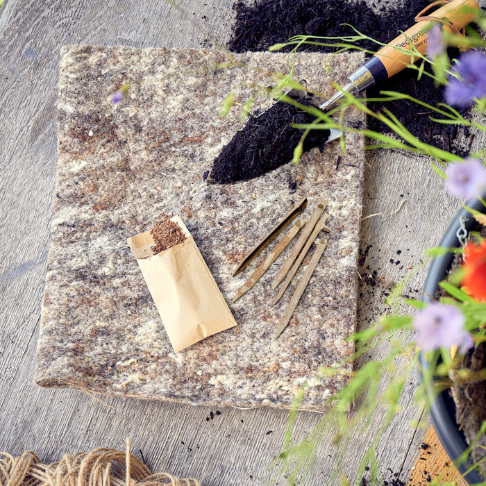 piece of sheep wool garden felt with bamboo pegs, seeds, and a trowel full of compost