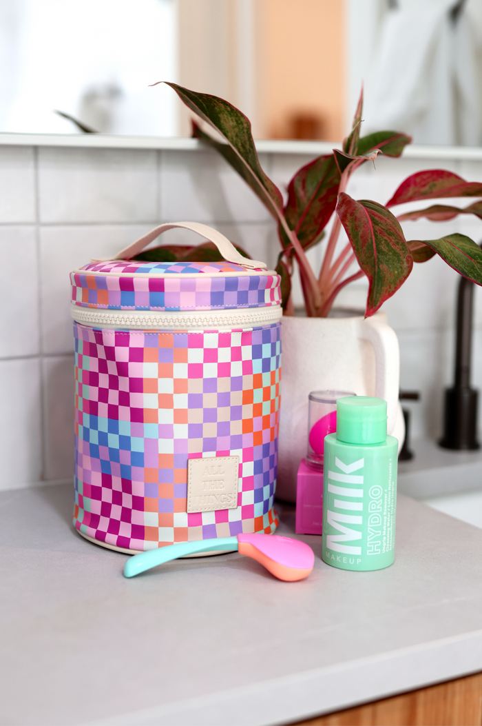 Colorful checkered makeup bag with pink and purple design, featuring zip closure and handle, perfect for travel.