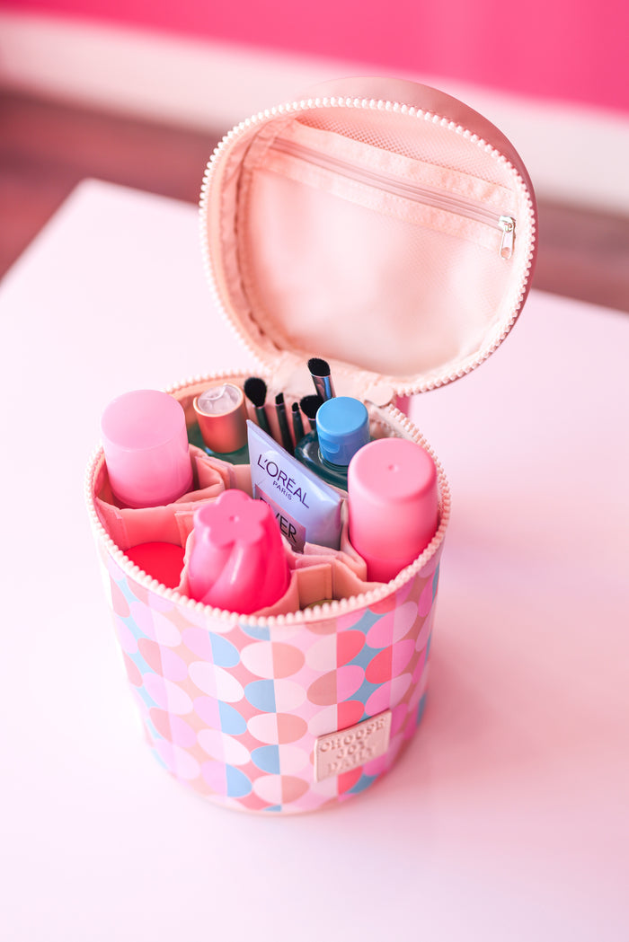 Pink round cosmetic bag with various beauty products, including bottles and brushes, organized neatly inside.