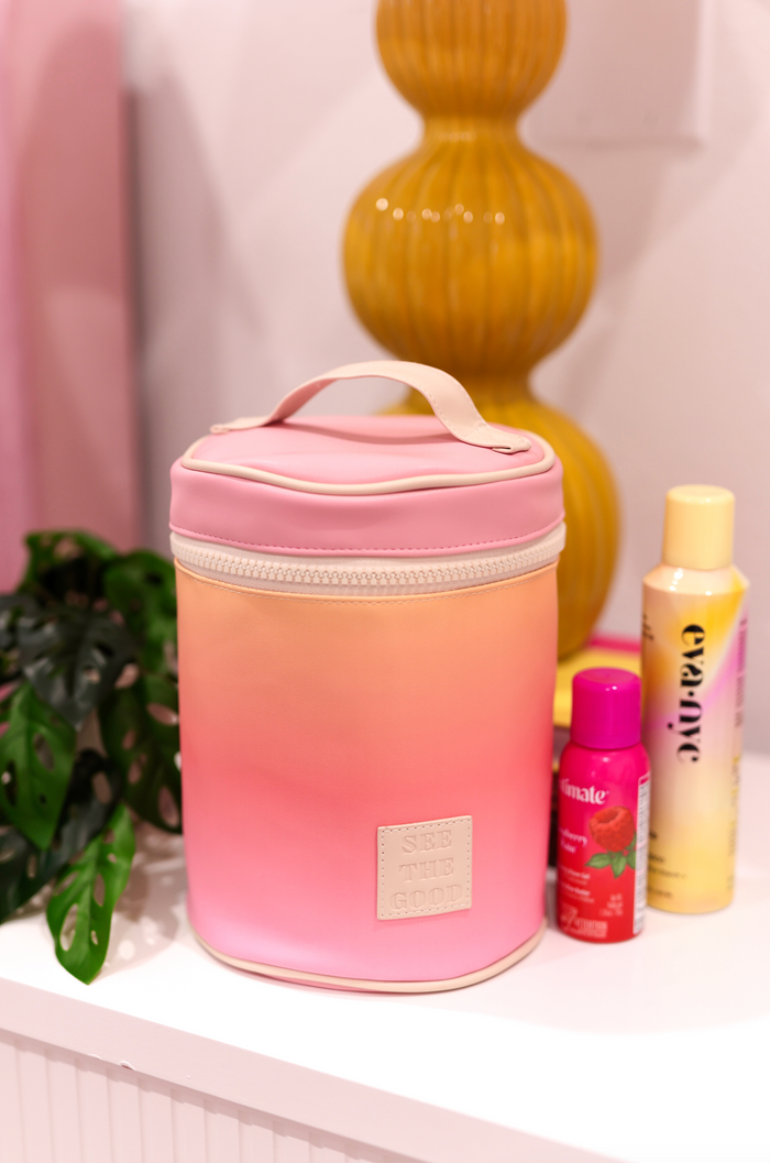Pink gradient cosmetic bag with zipper, featuring 'See The Good' label, ideal for storing beauty products.