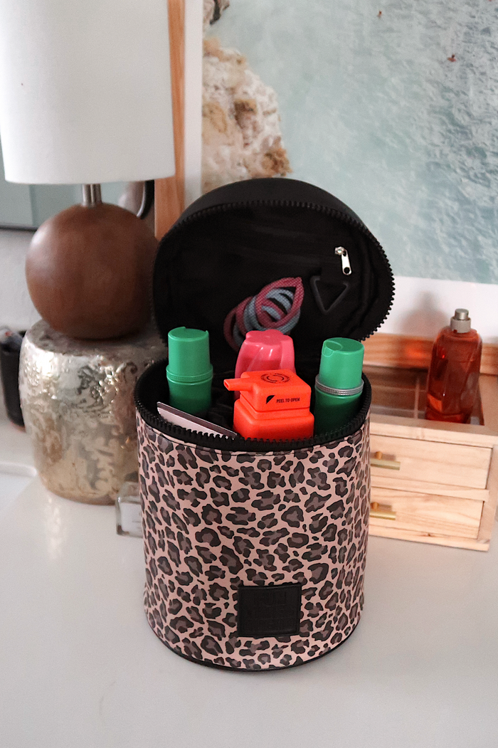 Pink leopard print cosmetic bag with zipper, holding various beauty products and accessories.