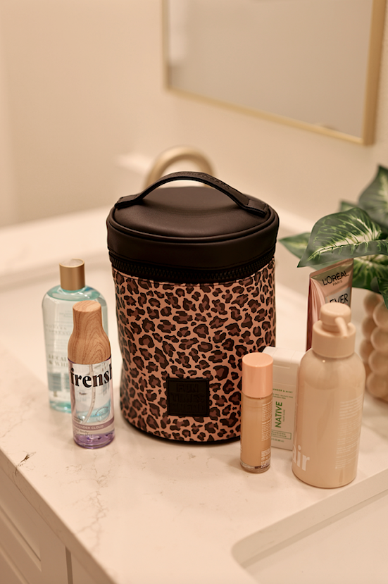 Leopard print beauty bag in black, stylish and spacious, surrounded by skincare products on a marble countertop.