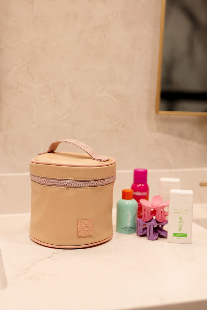 Beige cosmetic bag on a bathroom counter with various products