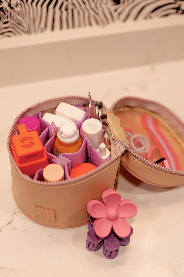 Blush cosmetic bag with organized beauty essentials and purple flower clips on a marble surface.