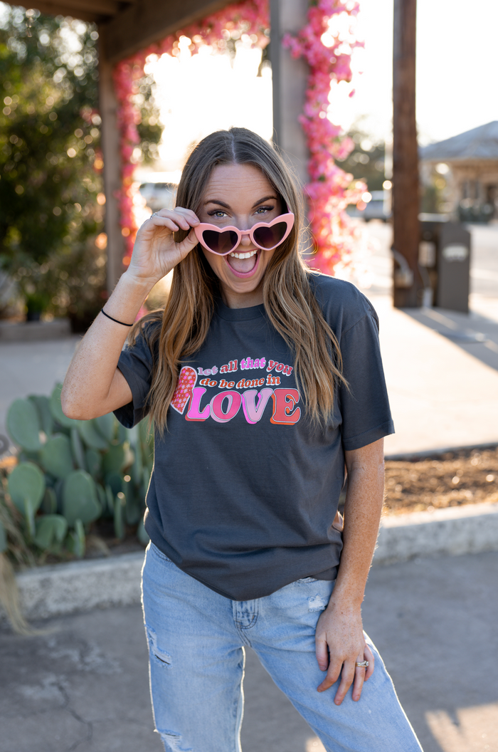 Woman wearing a gray graphic t-shirt with 'Love' print and pink heart sunglasses, outdoors.