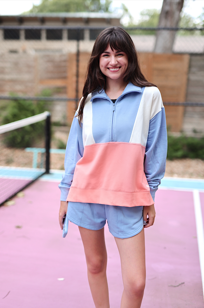 Stylish color-blocked women's athletic outfit in blue and peach, featuring a zip-up pullover and shorts.