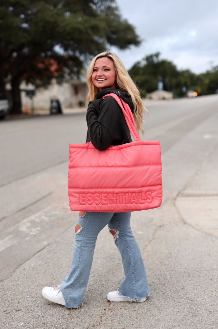 Bright pink puffer tote bag with 'ESSENTIALS' logo, stylish and padded for everyday use.
