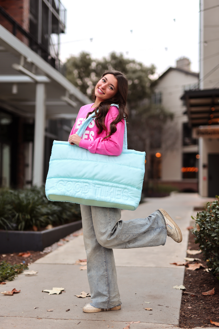 Light blue padded tote bag with 'GOOD TIMES' print, stylishly carried by woman in pink top and jeans.