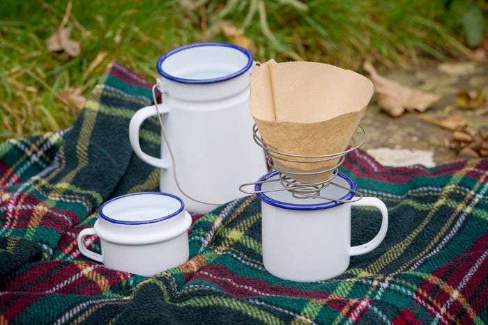 Portable wire coffee dripper with enamel mug and billycan on tartan picnic rug and autumn leaves
