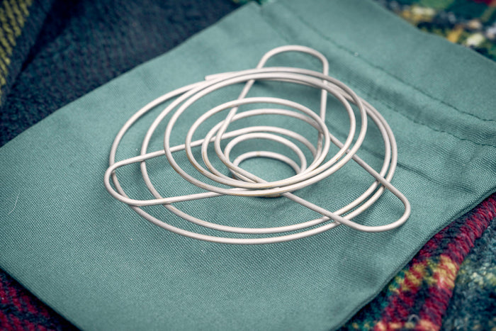 Portable wire coffee dripper collapsed flat, on top of green organic cotton carry pouch