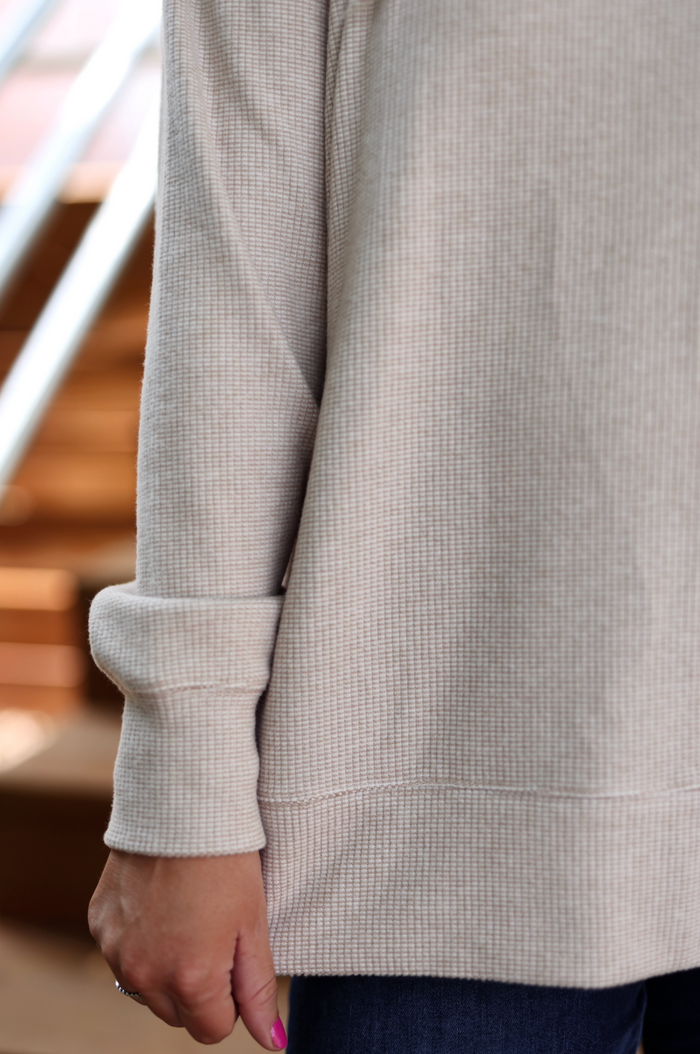Light beige waffle knit sweater with rolled cuffs, perfect for casual layering in cooler weather.