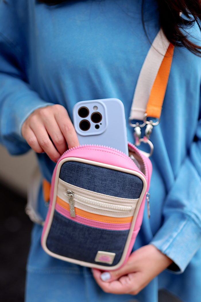 Colorful small crossbody bag in denim and pink with phone inside, featuring multiple zippered pockets.