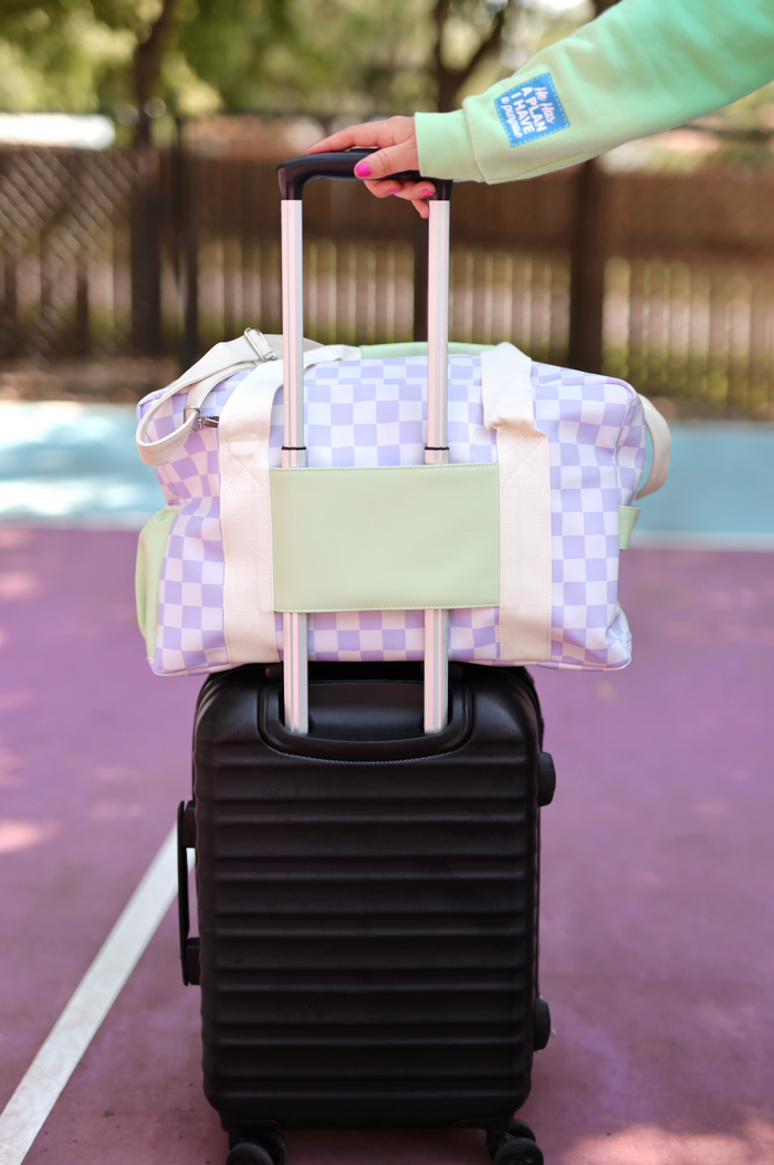Lavender checkered duffel bag on a black rolling suitcase, perfect for travel.