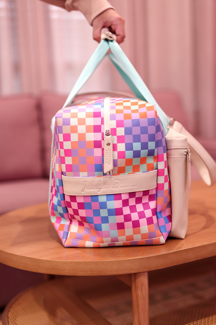 Colorful checkered duffle bag, pink, blue, and orange, made of durable material with stylish handles.