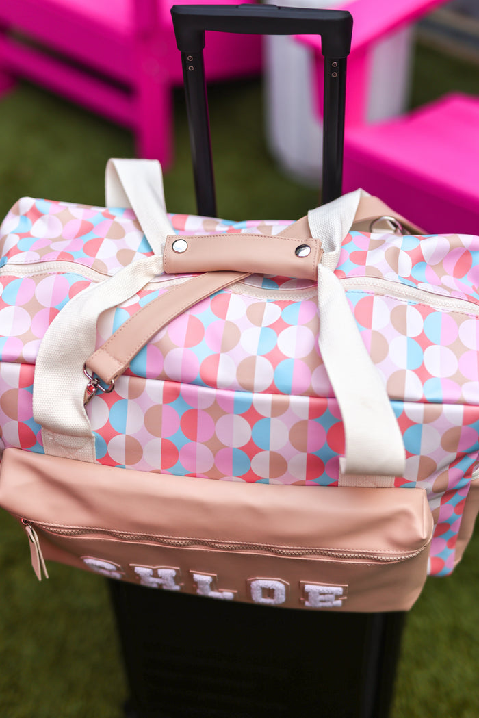 Colorful duffel bag with geometric pattern, beige accents, and a name tag, perfect for travel.