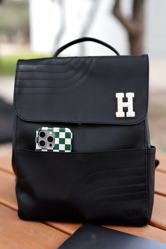 Black leather backpack with a textured design and a personalized 'H' emblem, featuring an exterior phone pocket.