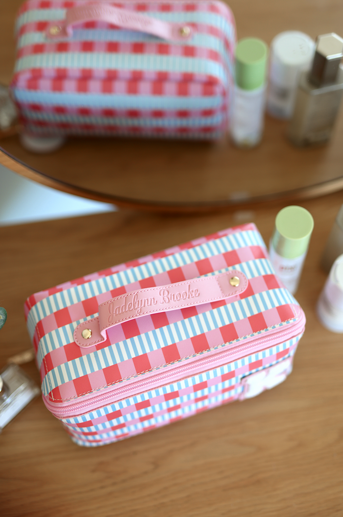 Colorful striped cosmetics bag in pink and blue with leather handle, perfect for makeup and skincare organization.
