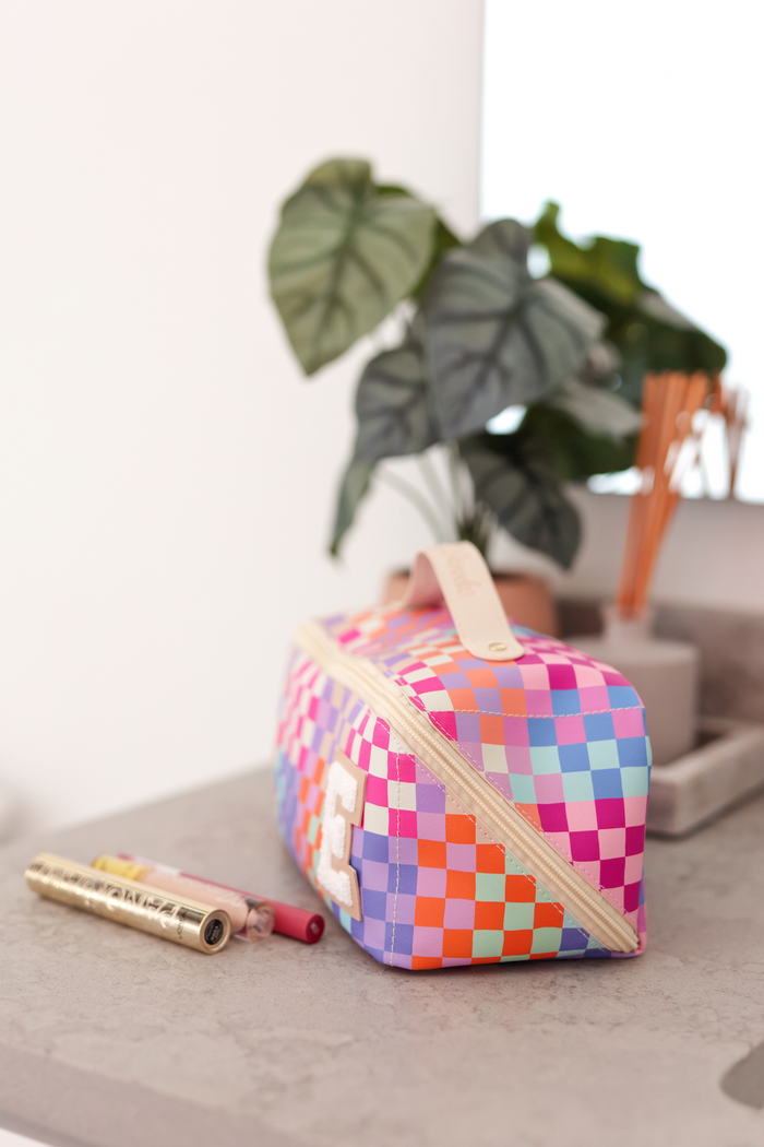 Colorful checkered makeup bag in pink, blue, and orange; features a zipper and decorative initial.