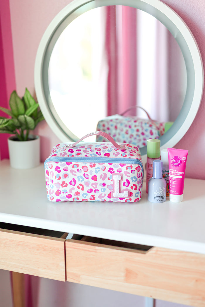 Pink cheetah print makeup bag on a vanity with mirror and skincare products.
