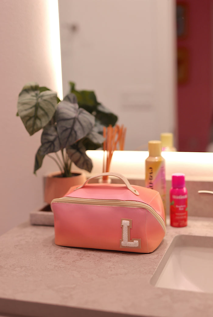 Personalized gradient pink cosmetic bag with L monogram, perfect for makeup storage and travel.
