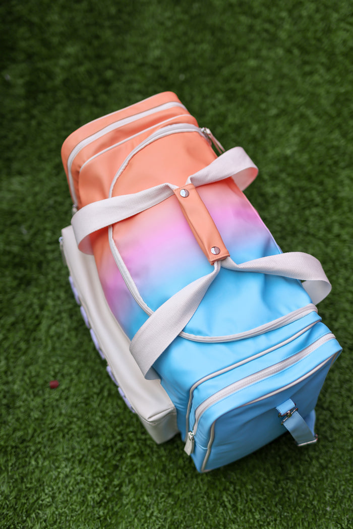 Gradient-colored bag with white straps on a green grass background