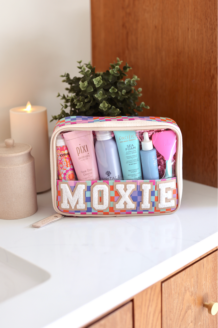 Colorful Moxie travel bag filled with skincare products on a marble countertop.
