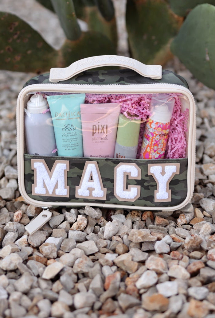 Camouflage cosmetic bag with skincare products, pink interior, personalized 'MACY' label, durable material.