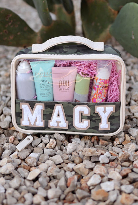 Camouflage cosmetic bag with skincare products, pink interior, personalized 'MACY' label, durable material.