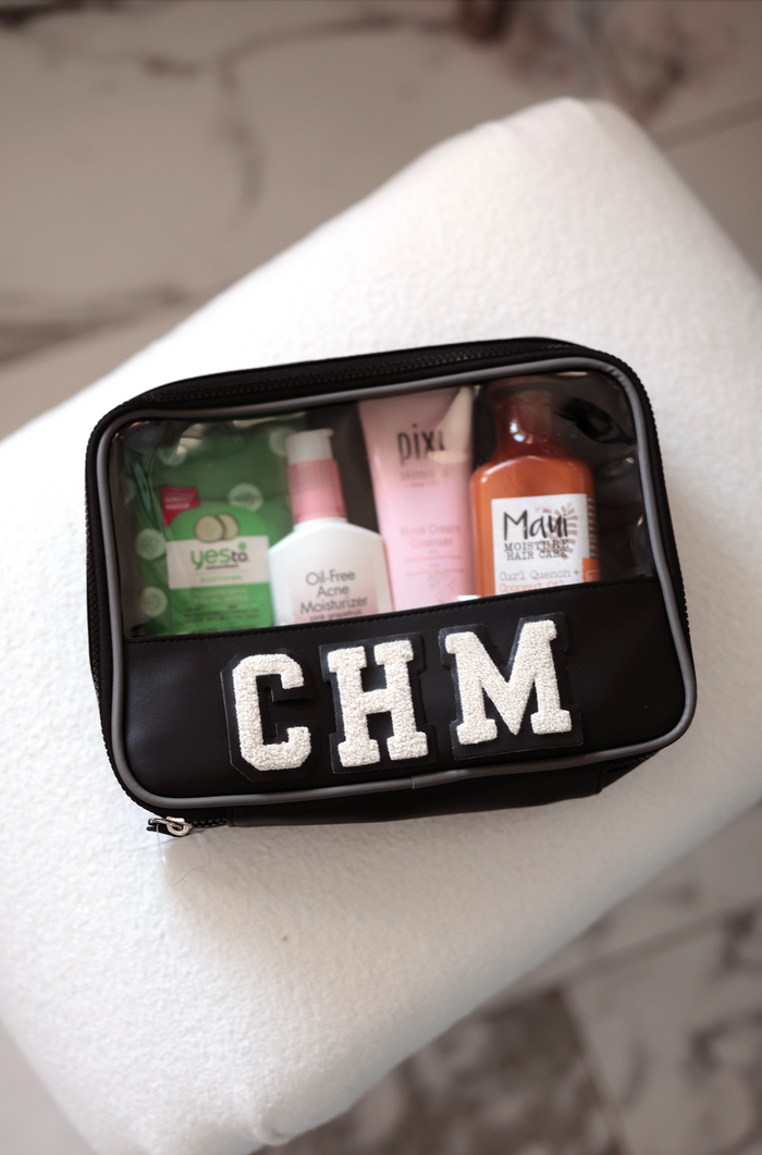 Black zippered cosmetic bag with clear top, featuring skincare products and initials CHM.