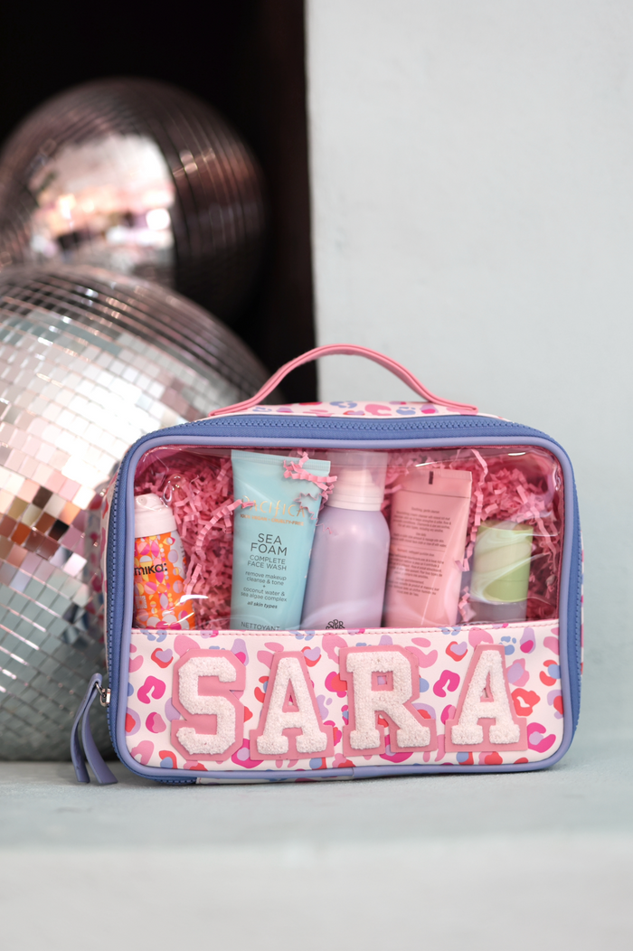 Personalized pink makeup bag containing skincare products, with clear window and playful leopard print design.
