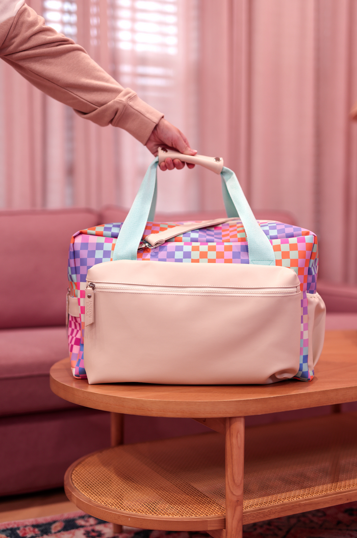 Colorful checkered weekender bag with light blue handles and a cream front pocket. Ideal for travel.
