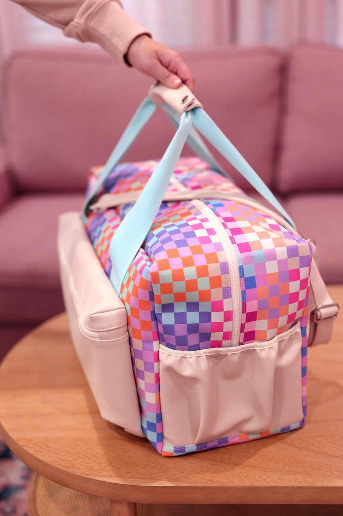 Colorful checkerboard duffel bag with light blue straps and cream bottom, ideal for travel and gym.