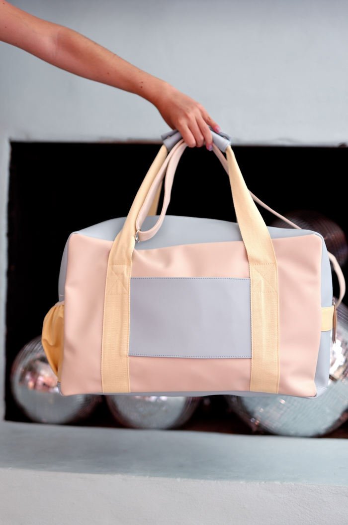 Stylish pastel duffel bag in pink, blue, and yellow, made from durable material for travel and gym use.