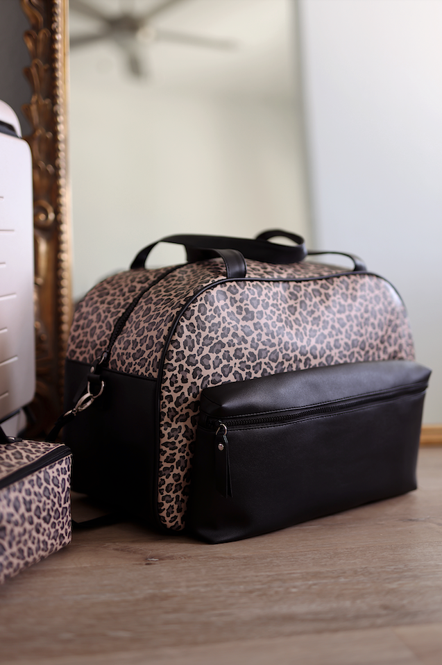 Stylish leopard print travel bag with black accents, featuring a zippered front pocket and sturdy handles.