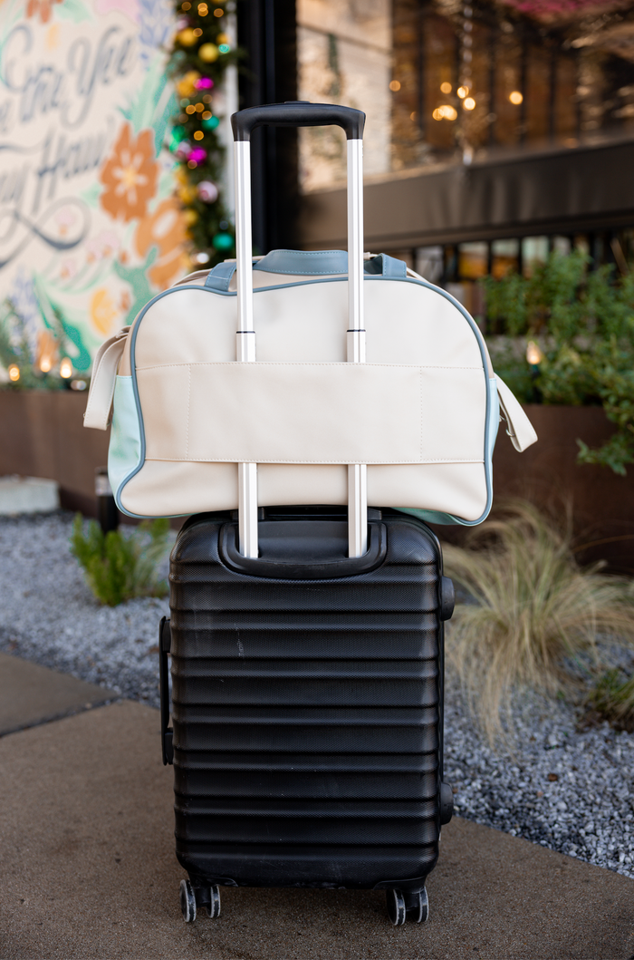 Stylish beige travel duffel bag on top of a black hard-shell suitcase with wheels.